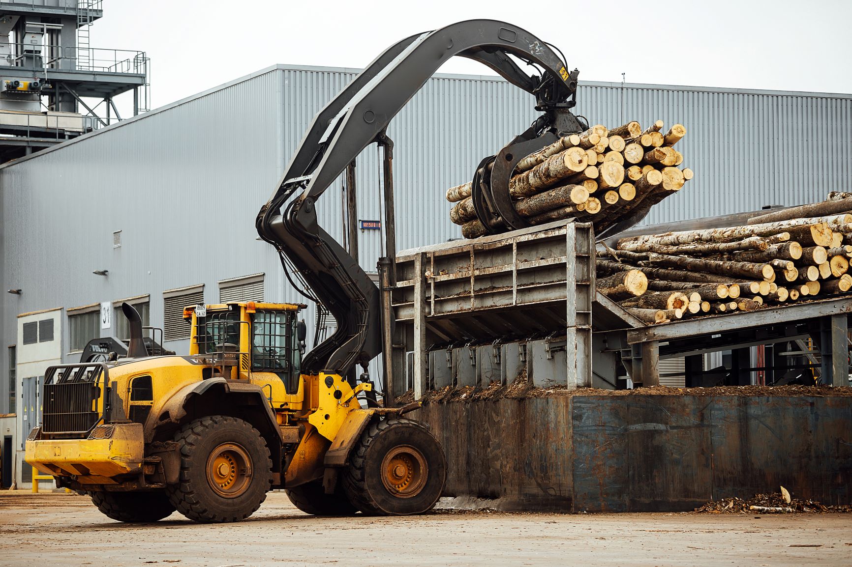 Industrial excavator with mechanical gripper transports wood in warehouse